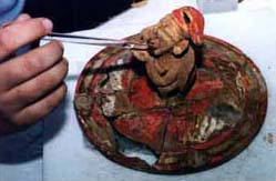Figure 2: In the field laboratory adjacent to the site, project conservator Lynn A. Grant applies a dilute consolidant to stabilize fragments of bright red slip on the surface of this modeled ceramic lid.
