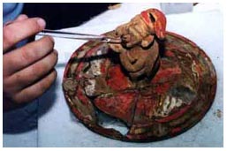 Figura 2: En el laboratorio de campo adyacente al sitio, la conservadora del proyecto, Lynn A. Grant, aplica un consolidante diluído para estabilizar los fragmentos de un slip rojo brillante sobre la superficie de esta tapa de cerámica modelada.