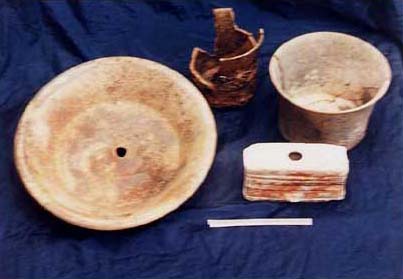 Figure 4a. Photo of the Teotihuac&aacute;n-style vessels from the Platform Group. Looking clockwise left to right shows an early slateware tripod dish with a storm god (Tlaloc?) image painted in red specular hematite paint, a blackware cylinder tripod with nubbin supports, a florero-like cylinder vase with an outflairing rim, and a black-on-orange single-hole candelero depicting a Maya-style temple. The scale is 13 cm.